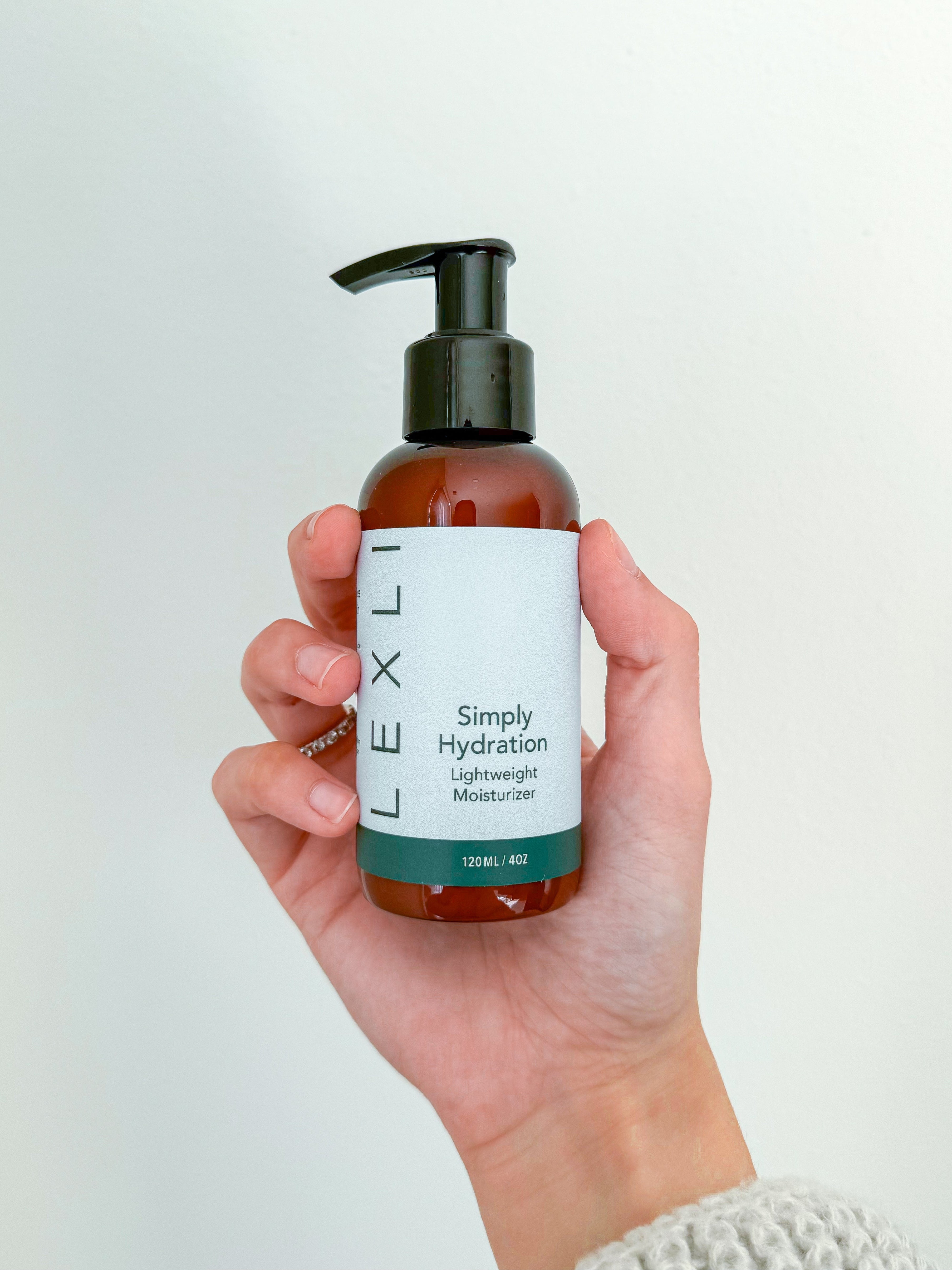 Photo of a hand holding a 4 ounce bottle of Lexli Simply Hydration lightweight face moisturizer.