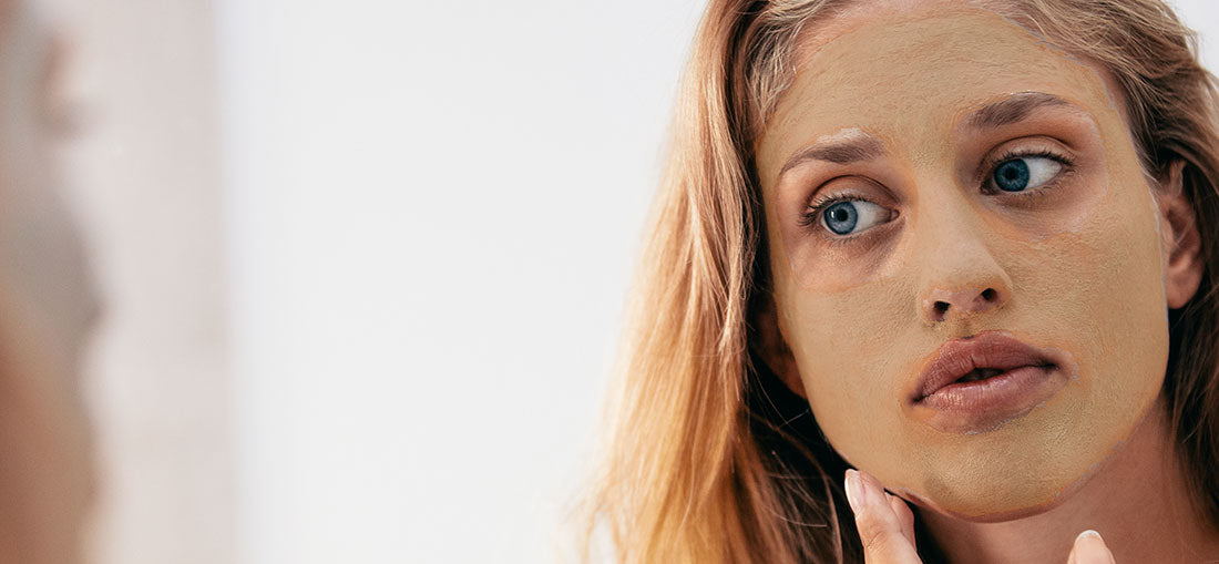 woman with face mask looking at her face in the mirror