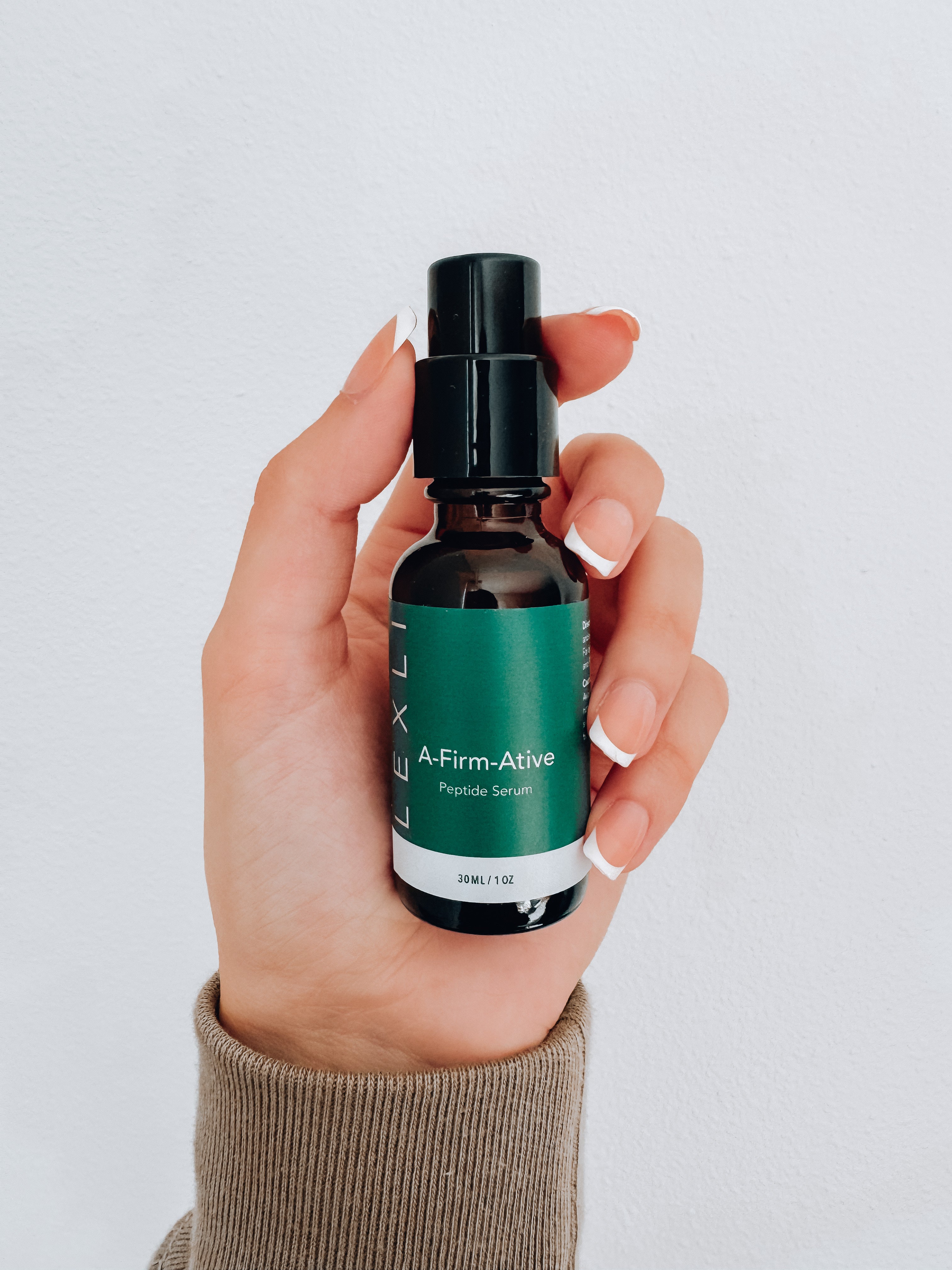 Photo of a hand holding a 1 ounce glass jar of A-Firm-Ative peptide serum.