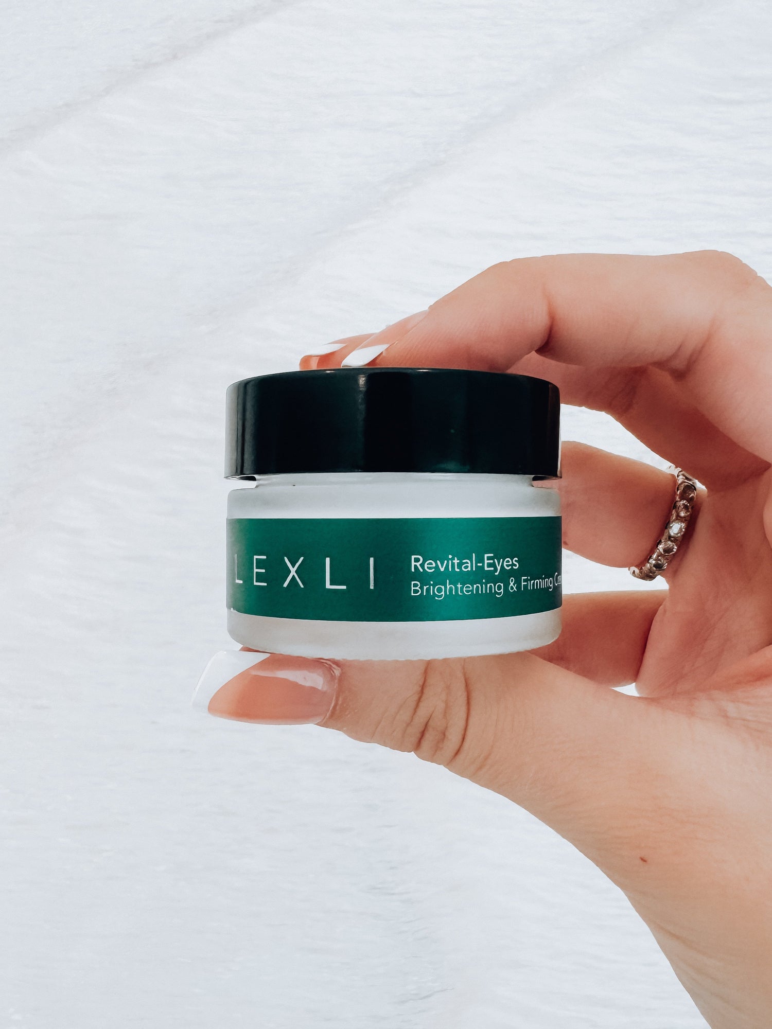 Photo of hand holding a .5 ounce jar of Lexli Revital-Eyes brightening and firming eye cream.