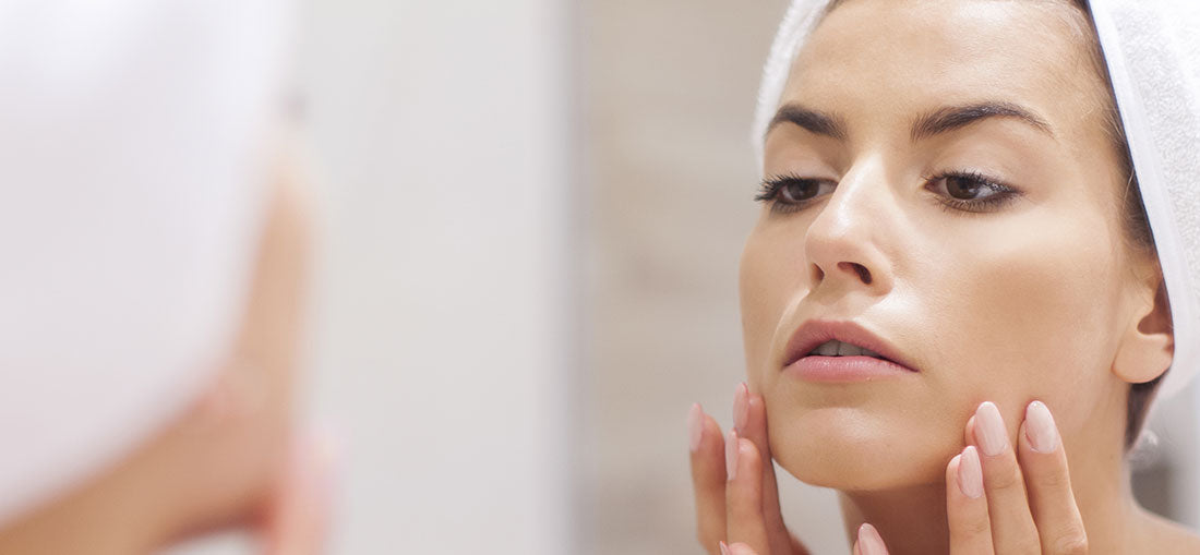woman with hands on face looking at her skin in the mirror