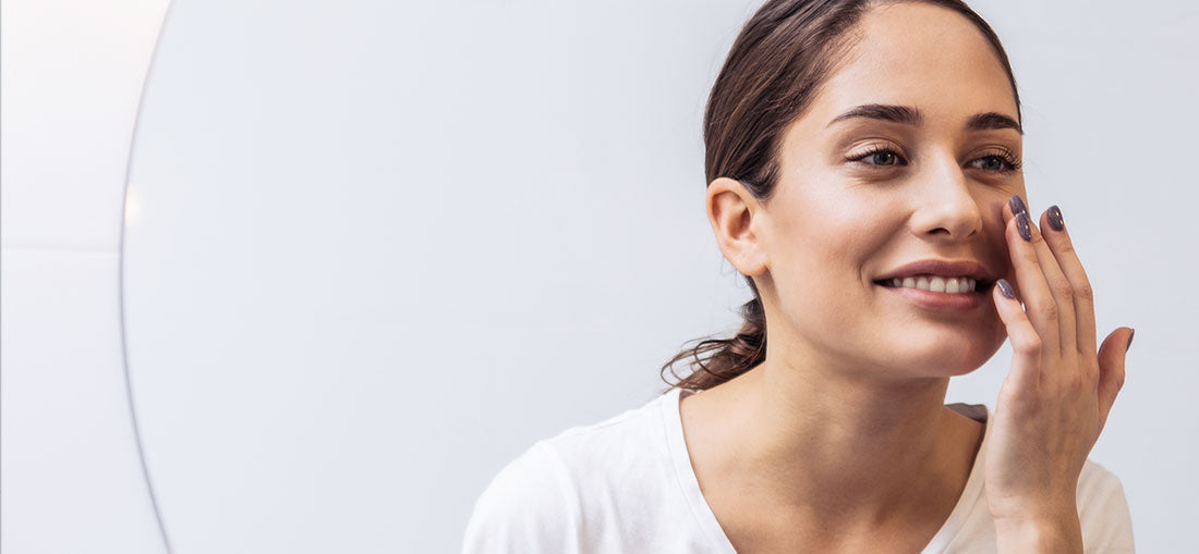 woman looking in mirror and smiling while applying product