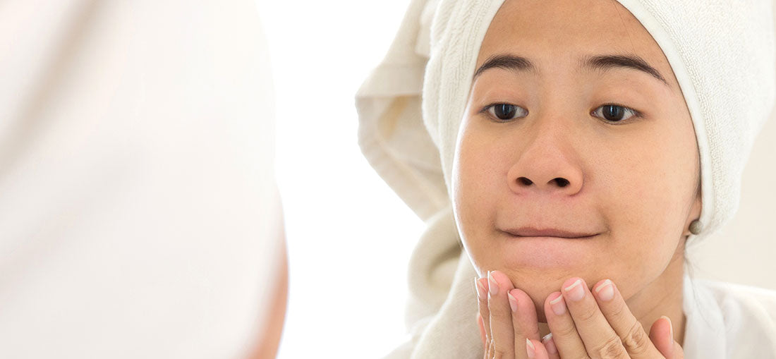 young woman looking at face in the mirror with hands on chin
