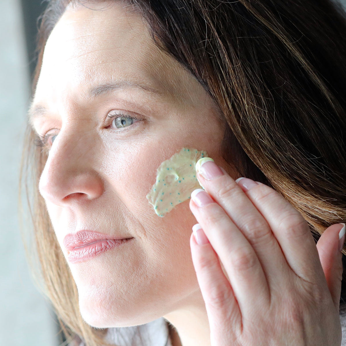 The side-view of woman applying AloeGlyC to her cheek with fingers.